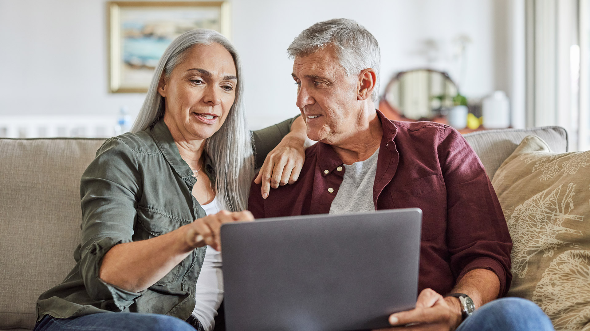 GettyImages-1283520768-1920px Medicare-aged couple sitting together on couch with laptop computer.