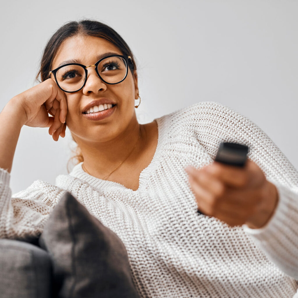 Young woman at home watching streaming content on a TV, holding a remote as brand advertising plays on the screen.