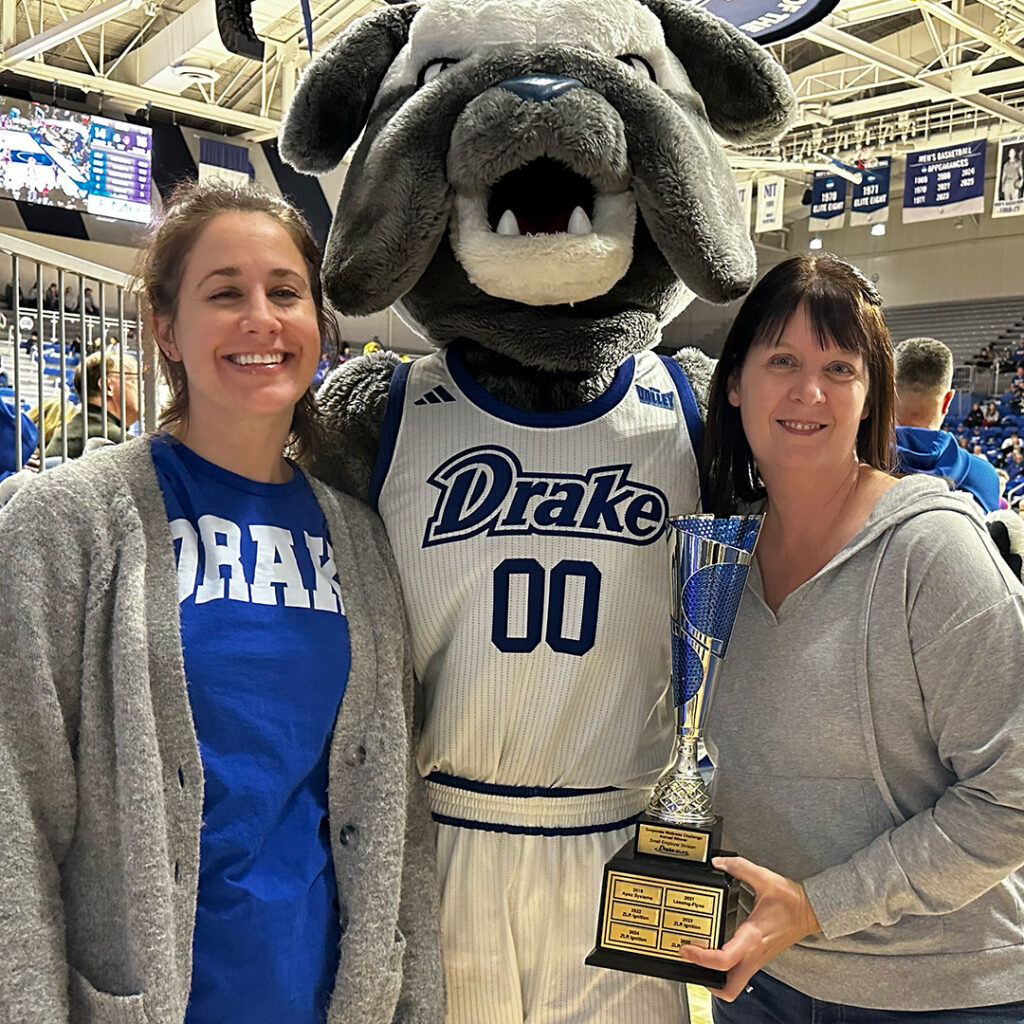 Two women holding the Drake Relays Wellness challenge award posing with Drake University's mascot, Spike.
